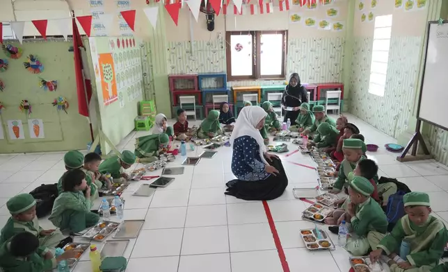 Students sit on the floor as they have their meals during the kick off of President Prabowo Subianto's ambitious free meal program to feed children and pregnant women nationwide despite critics saying that its required logistics could hurt Indonesia's state finances and economy at Early Childhood Education and Development in Jakarta, Indonesia, Monday, Jan. 6, 2025. (AP Photo/Achmad Ibrahim)