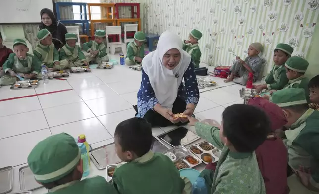 Students sit on the floor as they have their meals during the kick off of President Prabowo Subianto's ambitious free meal program to feed children and pregnant women nationwide despite critics saying that its required logistics could hurt Indonesia's state finances and economy at Early Childhood Education and Development in Jakarta, Indonesia, Monday, Jan. 6, 2025. (AP Photo/Achmad Ibrahim)