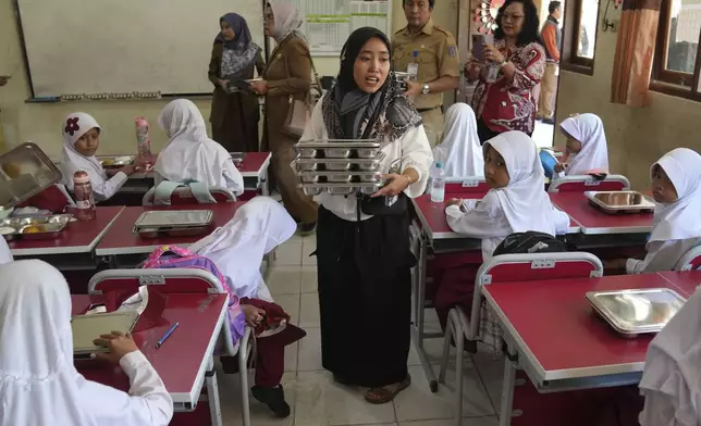 A member of school committee distributes meals to students during the kick off of President Prabowo Subianto's ambitious free meal program to feed children and pregnant women nationwide despite critics saying that its required logistics could hurt Indonesia's state finances and economy, at an elementary school in Depok, West Java, Indonesia, Monday, Jan. 6, 2025. (AP Photo/Dita Alangkara)