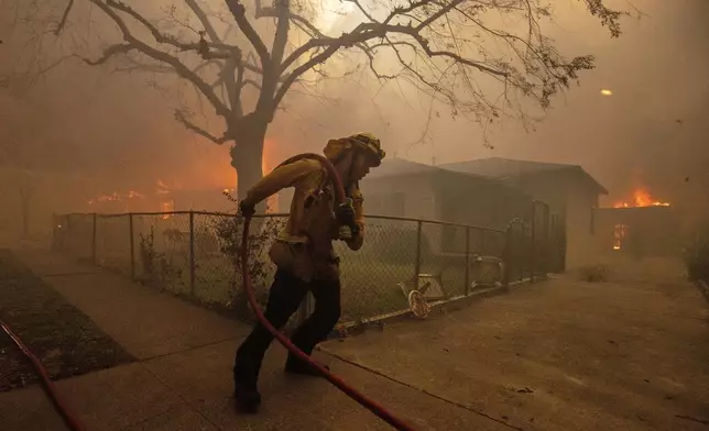 A firefighter protects a structure as the Eaton Fire advances Wednesday, Jan. 8, 2025 in Altadena, Calif. (AP Photo/Ethan Swope)