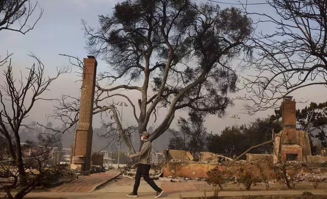 A person walks past a fire-ravaged property after the Palisades Fire swept through in the Pacific Palisades neighborhood of Los Angeles, Wednesday, Jan. 8, 2025. (AP Photo/Etienne Laurent)