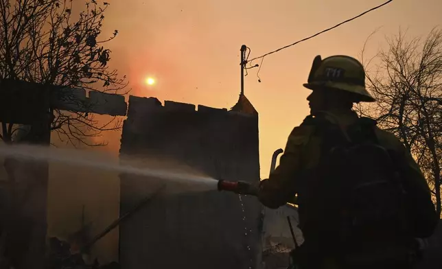 A firefighters waters down a home after the Eaton Fire burns in Altadena, Calif., Thursday, Jan. 9, 2025. (AP Photo/Nic Coury)