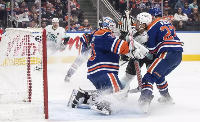 Seattle Kraken's John Hayden, center, and Edmonton Oilers' Brett Kulak (27) crash onto Oilers goalie Calvin Pickard, left, during first-period NHL hockey game action in Edmonton, Alberta, Monday, Jan. 27, 2025. (Jason Franson/The Canadian Press via AP)