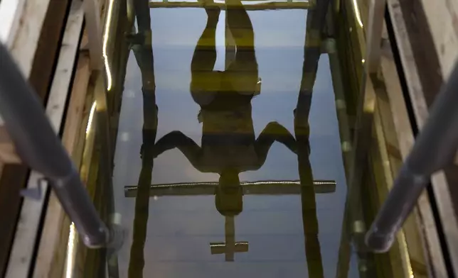 A man steps down to plunge as a cross is reflected in icy water before celebrating the Orthodox Epiphany in the Stroginskaya floodplain in Moscow, Russia, on Sunday, Jan. 19, 2025. (AP Photo/Alexander Zemlianichenko)