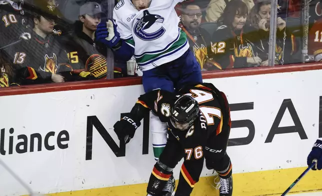 Vancouver Canucks' Noah Juulsen, top, is checked by Calgary Flames' Martin Pospisil (76) during the third period of an NHL hockey game in Calgary, Alberta, Tuesday, Dec. 31, 2024. (Jeff McIntosh/The Canadian Press via AP)