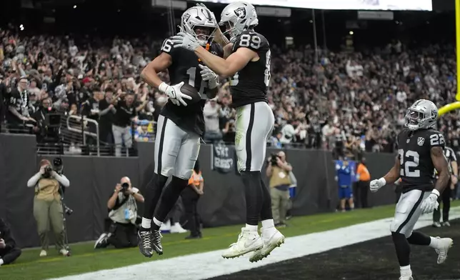 Las Vegas Raiders wide receiver Jakobi Meyers, middle left, is congratulated by tight end Brock Bowers after scoring against the Los Angeles Chargers during the first half of an NFL football game in Las Vegas, Sunday, Jan. 5, 2025. (AP Photo/John Locher)