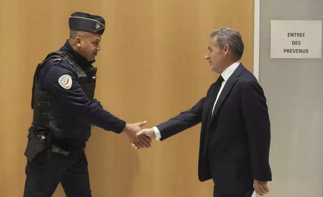 Former French President Nicolas Sarkozy shakes hands to a police officer as he arrives to the courtroom as he goes on trial over alleged illegal financing of his 2007 presidential campaign by the government of late Libyan leader Moammar Gadhafi, Monday, Jan. 6, 2025 in Paris. (AP Photo/Thibault Camus)