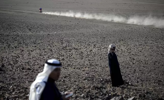 A competitor rides past local people during the prologue of the Dakar Rally in Bisha, Saudi Arabia, Friday, Jan. 3, 2025. (AP Photo/Christophe Ena)