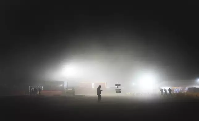 People walk in the dust in the base camp on the eve of the start of the Dakar Rally in Bisha, Saudi Arabia, Thursday, Jan. 2, 2025. (AP Photo/Christophe Ena)