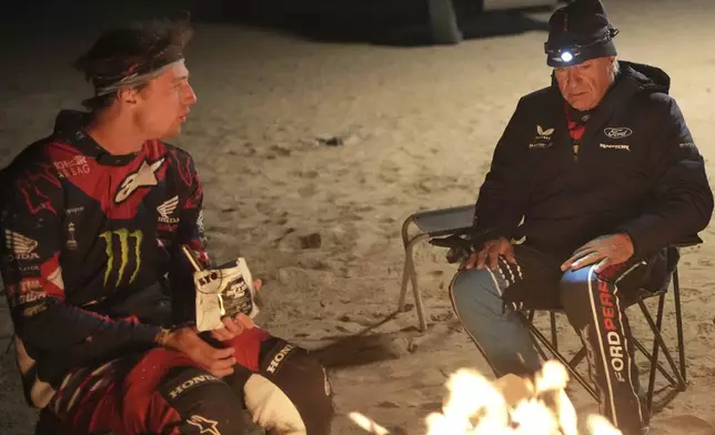 Driver Carlos Sainz speaks with rider Tosha Schareina at the bivouac after the stage two, day one, of the Dakar Rally with start in Bisha and finish in Bisha, Saudi Arabia, Sunday, Jan. 5, 2025. (AP Photo/Christophe Ena)
