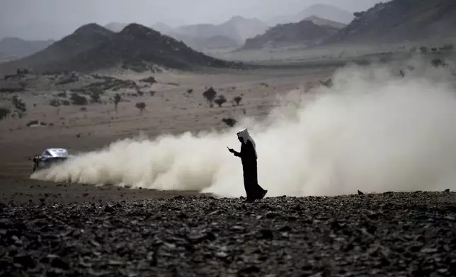 A man watches his phone during the prologue of the Dakar Rally in Bisha, Saudi Arabia, Friday, Jan. 3, 2025. (AP Photo/Christophe Ena)