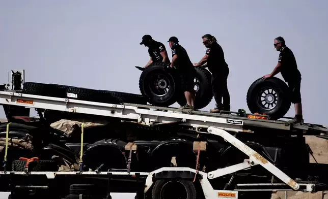 Mechanics carry wheels two days before the start of the Dakar Rally in Bisha, Saudi Arabia, Wednesday, Jan. 1, 2025. (AP Photo/Christophe Ena)