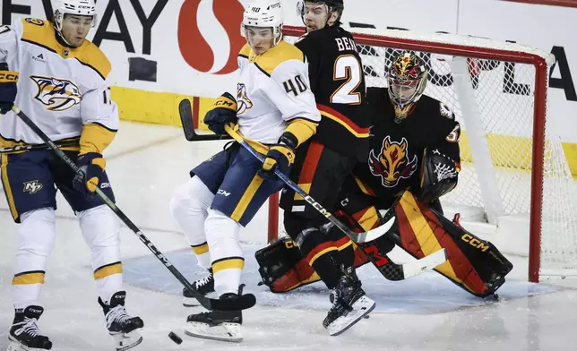 Nashville Predators' Mark Jankowski (17) tries to deflect the puck past Calgary Flames goalie Dustin Wolf, right, as Jake Bean, second right, checks Fedor Svechkov (40) during the third period of an NHL hockey game in Calgary, Alberta, Saturday, Jan. 4, 2025. (Jeff McIntosh/The Canadian Press via AP)