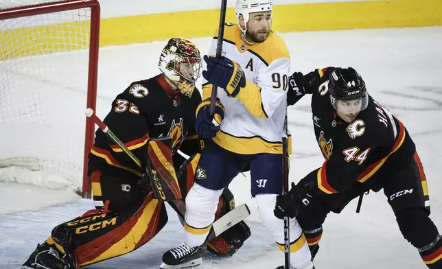 Nashville Predators' Ryan O'Reilly, center, is checked by Joel Hanley, right, as goalie Dustin Wolf looks on Calgary Flames' during the second period of an NHL hockey game in Calgary, Alberta, Saturday, Jan. 4, 2025. (Jeff McIntosh/The Canadian Press via AP)