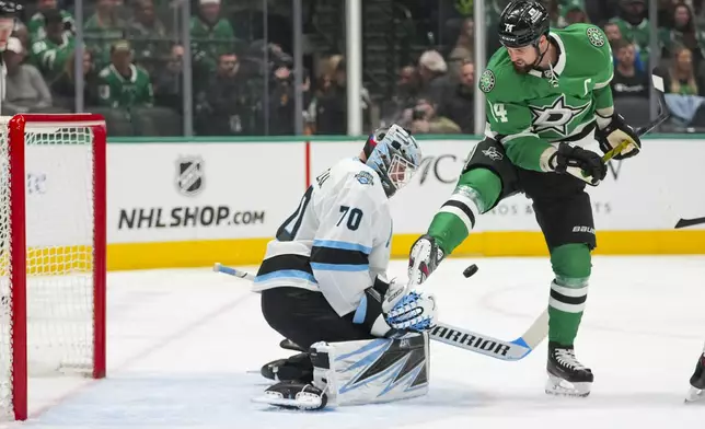 Utah Hockey Club goaltender Karel Vejmelka (70) deflects the puck as Dallas Stars left wing Jamie Benn (14) attacks during the first period of an NHL hockey game, Saturday, Jan. 4, 2025, in Dallas. (AP Photo/Julio Cortez)