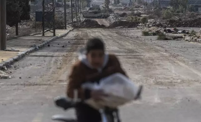 A boy carrying bread cycles home as Israeli military armored vehicles block a road leading to the town of Quneitra, Syria, Sunday, Jan. 5, 2025. (AP Photo/Mosa'ab Elshamy)