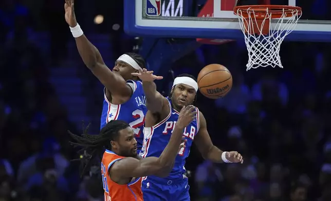 Oklahoma City Thunder's Cason Wallace, bottom, passes the ball against Philadelphia 76ers' Ricky Council IV, right, and Guerschon Yabusele during the first half of an NBA basketball game, Tuesday, Jan. 14, 2025, in Philadelphia. (AP Photo/Matt Slocum)