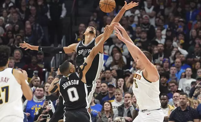 Denver Nuggets center Nikola Jokic, right, passes the ball as San Antonio Spurs forward Keldon Johnson, front left, and center Victor Wembanyama defend in the second half of an NBA basketball game Friday, Jan. 3, 2025, in Denver. (AP Photo/David Zalubowski)