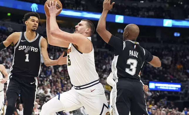 Denver Nuggets center Nikola Jokic, center, drives to the basket between San Antonio Spurs center Victor Wembanyama, left, and guard Chris Paul in the first half of an NBA basketball game Friday, Jan. 3, 2025, in Denver. (AP Photo/David Zalubowski)