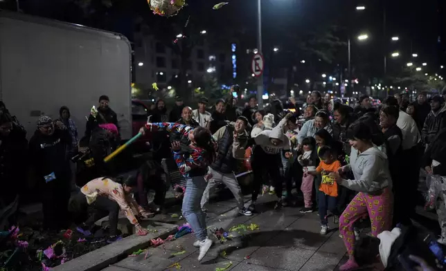 A woman strikes a traditional "pinata" donated by volunteers known as the Punk Kings who distribute toys, clothes and pinatas to underprivileged children on the occasion of the Epiphany, or Three Kings Day, in Mexico City, Sunday, Jan. 5, 2025. (AP Photo/Eduardo Verdugo)