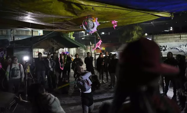 A woman strikes a traditional "pinata" donated by volunteers who call themselves Los Punk Kings who distribute toys, clothes and pinatas to underprivileged children at a migrant shelter on the occasion of the Epiphany, or Three Kings Day, in Mexico City, early Monday, Jan. 6, 2025. (AP Photo/Eduardo Verdugo)