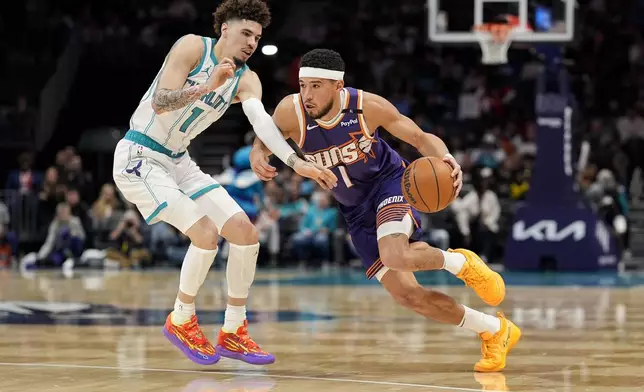 Phoenix Suns guard Devin Booker (1) drives to the basket against Charlotte Hornets guard LaMelo Ball (1) during the first half of an NBA basketball game in Charlotte, N.C., Tuesday, Jan. 7, 2025. (AP Photo/Jim Dedmon)