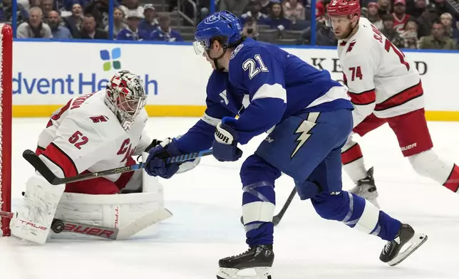 Tampa Bay Lightning center Brayden Point (21) shoots on Carolina Hurricanes goaltender Pyotr Kochetkov (52) and defenseman Jaccob Slavin (74) looks on during the second period of an NHL hockey game Tuesday, Jan. 7, 2025, in Tampa, Fla. (AP Photo/Chris O'Meara)