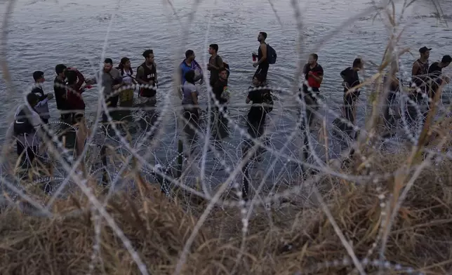 FILE - Migrants wait to climb over concertina wire after they crossed the Rio Grande and entered the U.S. from Mexico on Sept. 23, 2023, in Eagle Pass, Texas. (AP Photo/Eric Gay, File)