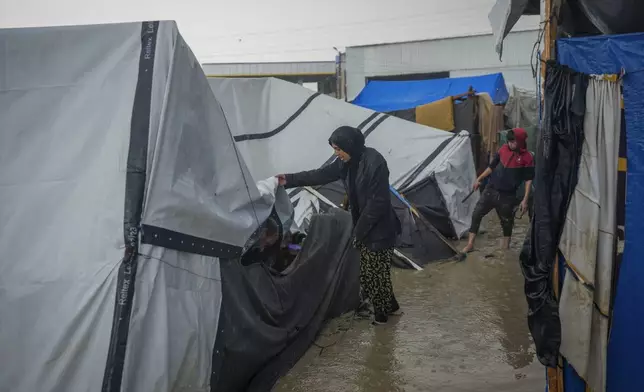 Manal Lubbad, a 49-year-old mother of eight and a displaced woman from Gaza City, tries to repair her flooded and damaged tent after heavy overnight rainfall at the refugee tent camp for displaced Palestinians in Deir al-Balah, central Gaza Strip, Tuesday, Dec. 31, 2024. (AP Photo/Abdel Kareem Hana)