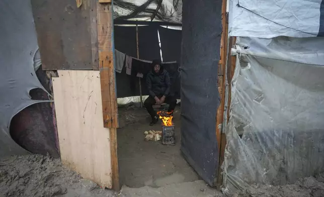 A man warms himself by a small fire inside a makeshift tent following overnight rainfall at the refugee tent camp for displaced Palestinians in Deir al-Balah, central Gaza Strip Tuesday, Dec. 31, 2024. (AP Photo/Abdel Kareem Hana)