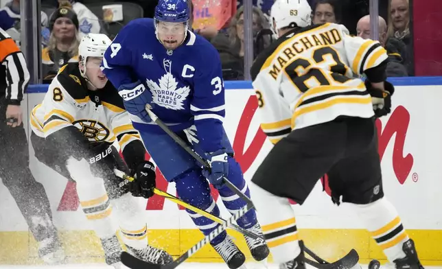 Toronto Maple Leafs center Auston Matthews (34) tries to move the puck between Boston Bruins defenseman Mason Lohrei (6) and teammate Brad Marchand (63) during the first period of an NHL hockey game in Toronto, Saturday, Jan. 4, 2025. (Frank Gunn/The Canadian Press via AP)