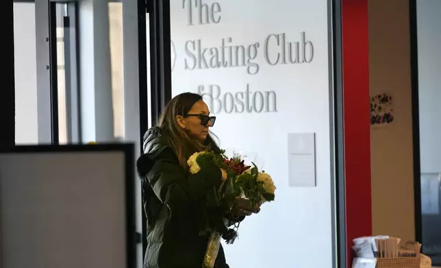 A woman brings flowers to The Skating Club of Boston, where six athletes, coaches and family associated with the club are believed to have perished in the collision of a passenger aircraft and military helicopter in Washington, Thursday, Jan. 30, 2025, in Norwood, Mass. (AP Photo/Robert F. Bukaty)