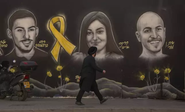 An Ultra-orthodox Jewish man walks past a graffiti that displays portraits of hostages held by Hamas in Gaza, in Jerusalem, on Monday, Jan. 13, 2025. (AP Photo/Ohad Zwigenberg)
