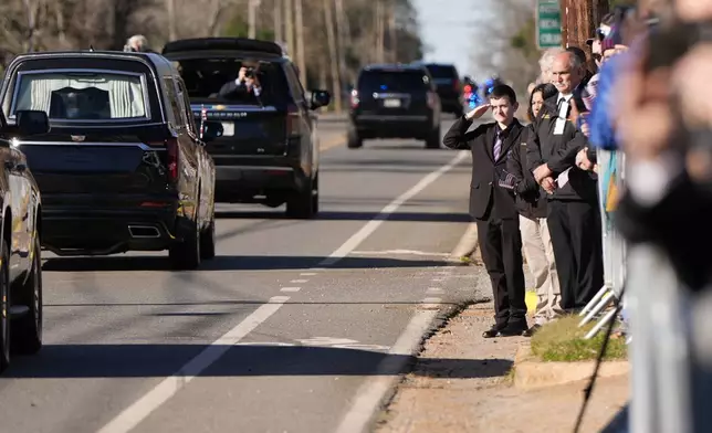 A young boy salutes as the hearse carrying the flag-draped casket of former President Jimmy Carter moves through downtown Plains, Ga., Saturday, Jan. 4, 2025. (AP Photo/Mike Stewart)