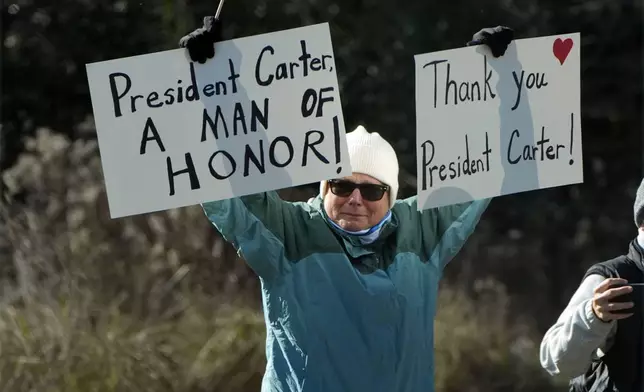 A person holds signs as the hearse containing the casket of former President Jimmy Carter, pauses at the Jimmy Carter Boyhood Farm in Archery, Ga., Saturday, Jan. 4, 2025. Carter died Dec. 29 at the age of 100. (AP Photo/Alex Brandon, Pool)