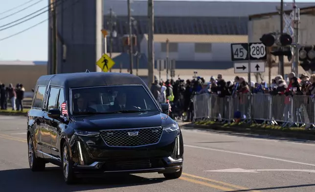 People watch as a hearse carrying the flag-draped casket of former President Jimmy Carter passes a grain elevator as it moves through downtown Plains, Ga., Saturday, Jan. 4, 2025. (AP Photo/Mike Stewart)