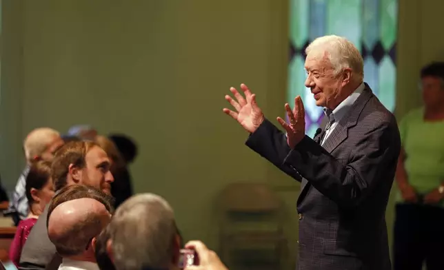 FILE - Former President Jimmy Carter welcomes visitors to Maranatha Baptist Church before teaching Sunday school in Plains, Ga., June 8, 2014. (AP Photo/John Bazemore, File)