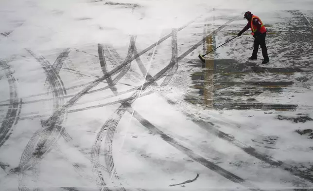 A worker clears snow from an apron before guiding a Delta Air Lines jet at the Detroit Metropolitan Wayne County Airport in Romulus, Mich., Monday, Jan. 6, 2025. (AP Photo/Charlie Riedel)