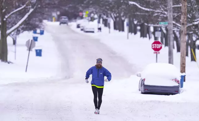 A runner makes his way through a snow-covered street in Indianapolis, Monday, Jan. 6, 2025. (AP Photo/Michael Conroy)