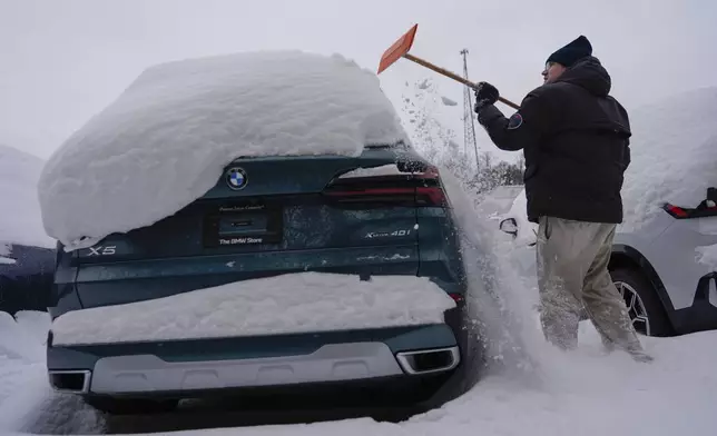 Cary Fallath, the BMW Store lot technician, clears snow from new cars in Silverton, Ohio, Tuesday, Jan. 7, 2025. (AP Photo/Carolyn Kaster)