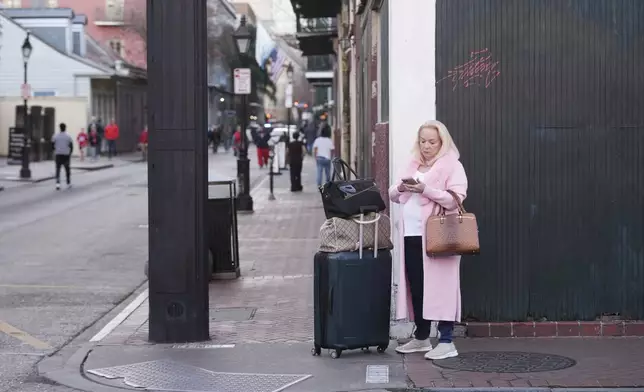 Liz Cowart uses her phone to call a car to the airport from the French Quarter after a vehicle drove into a crowd on New Orleans' Canal and Bourbon Street, Wednesday Jan. 1, 2025. (AP Photo/Gerald Herbert)