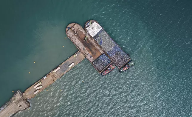 Workers load sacks of wood pellets onto barges at a port in Pohuwato, Gorontalo province, Indonesia, Tuesday, Oct. 22, 2024. (AP Photo/Yegar Sahaduta Mangiri)