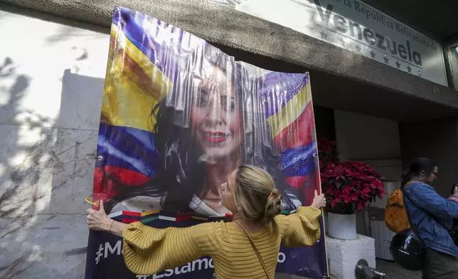An opponent of Venezuelan President Nicolas Maduro hangs up an image of opposition leader Maria Corina Machado outside the Venezuelan embassy in Mexico City, Thursday, Jan. 9, 2024, a day before Maduro's inauguration for a third term. (AP Photo/Fernando Llano)