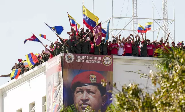 Military and government supporters wave from the roof of the presidential guard headquarters as Venezuelan President Nicolas Maduro speaks at the presidential palace in Caracas, Venezuela, Friday, Jan. 10, 2025, on his inauguration day for a third term. The banner shows Maduro's predecessor, the late President Hugo Chavez. (AP Photo/Matias Delacroix)