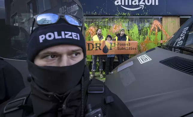 Activists of Drop Fossil Subsidies protest after they sprayed an Amazon shop window with paint as a police officer cordons off the area during the 55th annual meeting of the World Economic Forum, WEF, in Davos, Switzerland, Monday, Jan. 20, 2025. (Michael Buholzer/Keystone via AP)