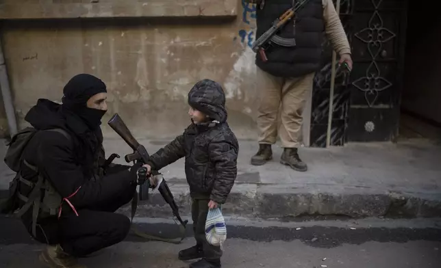 A member of the new security forces shakes hands with a boy during an operation to detain men suspected of being part of militias or loyalist soldiers of the ousted president Bashar Assad in Homs, Syria, Friday, Jan. 3, 2025. (AP Photo/Leo Correa)