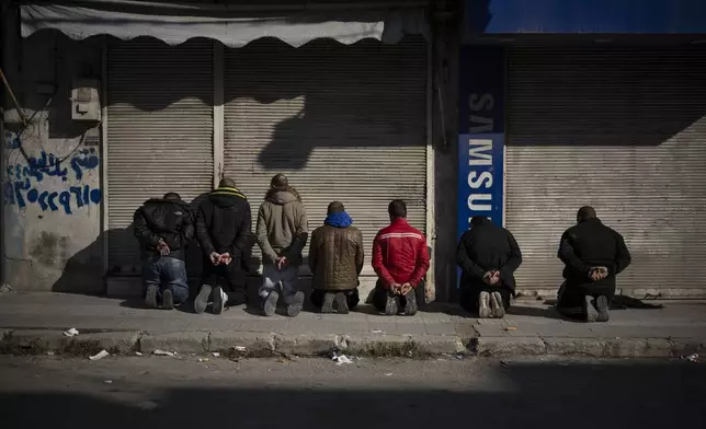 Detained men kneel down on the sidewalk as members of the new security forces take part in an operation to detain suspected people of being part of militias or loyalist soldiers of the ousted president Bashar Assad in Homs, Syria, Friday, Jan. 3, 2025. (AP Photo/Leo Correa)