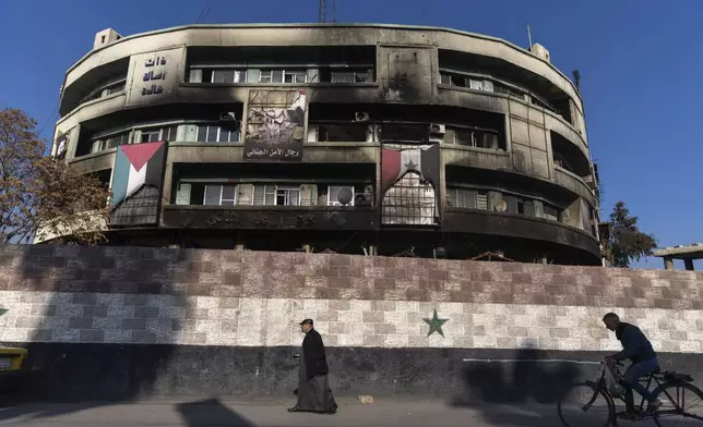 People walk past a security building that belonged to the Assad regime which was burned during the rebel takeover, in Damascus, Syria, Friday, Jan. 3, 2025. (AP Photo/Mosa'ab Elshamy)