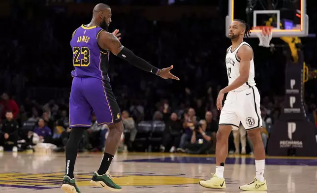 Los Angeles Lakers forward LeBron James, left, gestures toward fans after hitting a three-point shot as Brooklyn Nets forward Tosan Evbuomwan watches during the first half of an NBA basketball game, Friday, Jan. 17, 2025, in Los Angeles. (AP Photo/Mark J. Terrill)