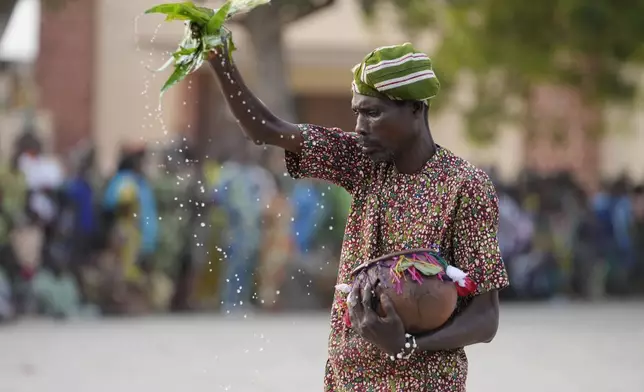A man sprinkles water as Zangbeto masquerades the traditional Voodoo guardians of the night performing ahead of the annual Voodoo Festival in Ouidah, Benin, Thursday, Jan. 9, 2025. (AP Photo/Sunday Alamba)